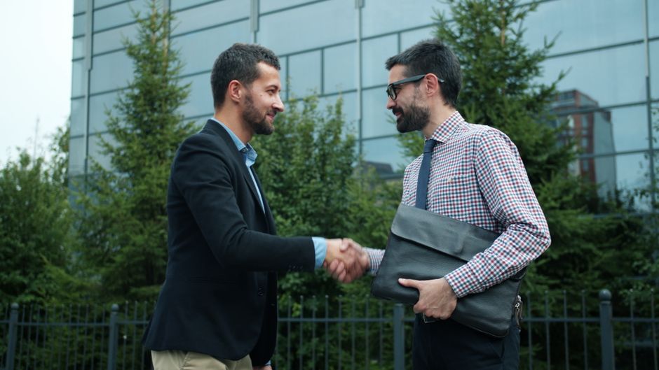Two businessmen shaking hands outside a modern office building, symbolizing partnership