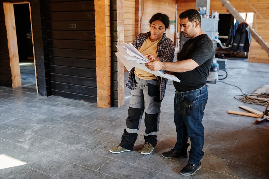 Two workers examining blueprints inside a building under construction